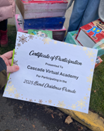 A hand is holding a certificate of participation for one of the schools involved in the 2026 Bend Christmas Parade 